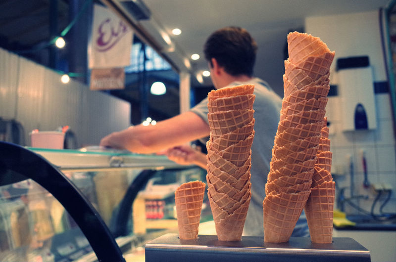 Close-up of stacked ice cream cones by man in parlor