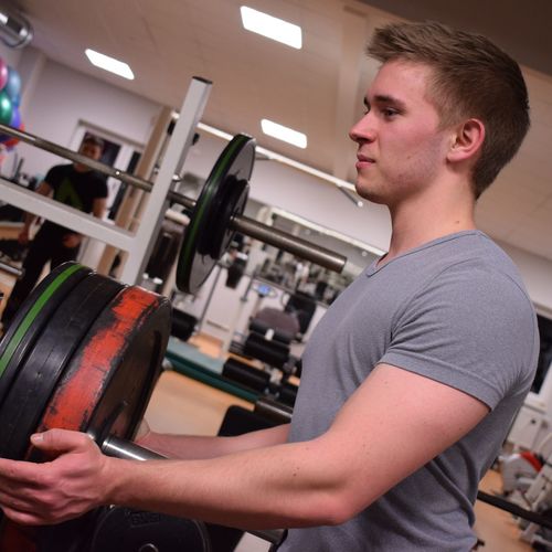 Side view of young man looking away while holding weights in gym