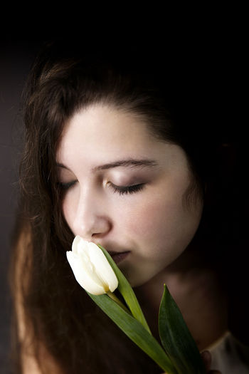 Close-up of young woman kissing flower in darkroom