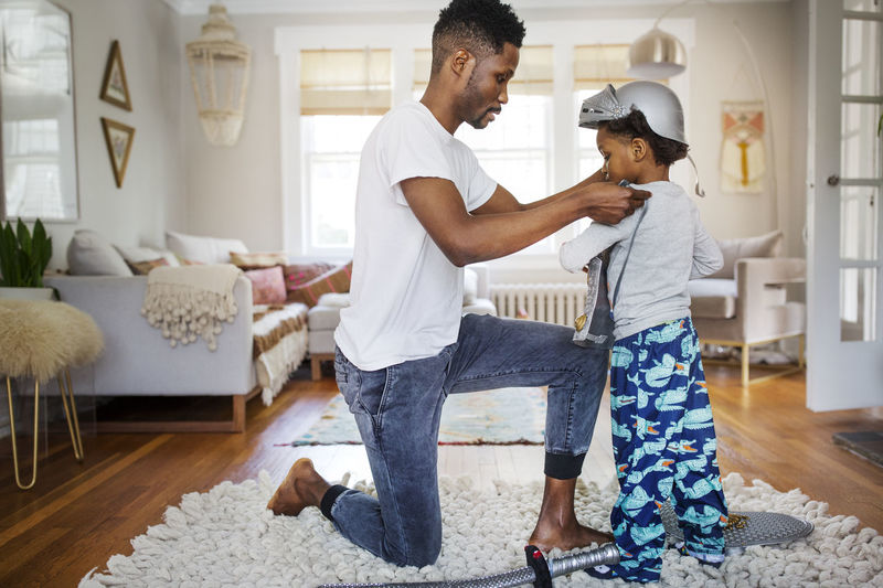 Father putting suit of armor on boy at home