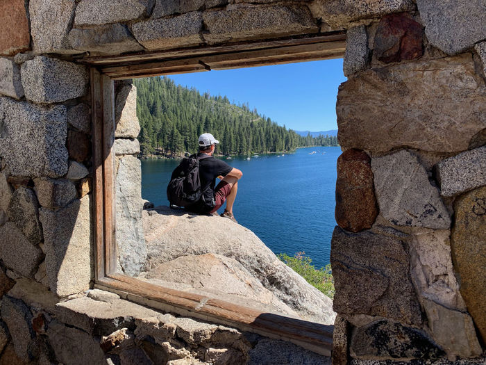 Man sitting on rock by lake framed by window