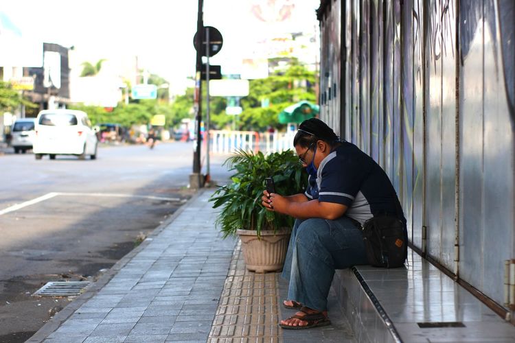 Side view of man sitting on street in city