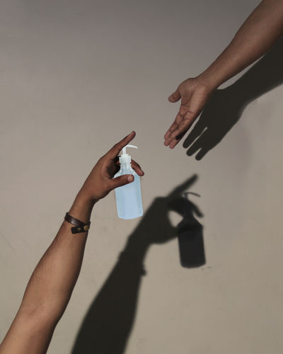Cropped hand giving hand sanitizer against wall
