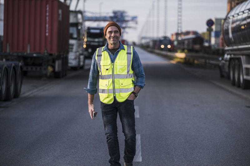 Smiling male truck driver with hand in pocket walking on street at dock