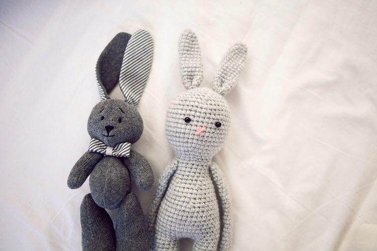 Two knitted rabbit toys lie under a blanket in a white bed