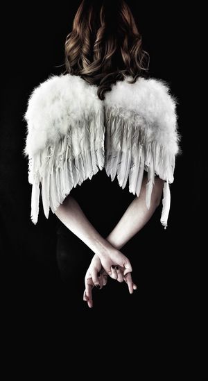 Rear view of woman wearing angel costume against black background