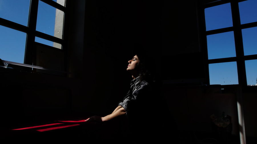 Side view of young man meditating in darkroom
