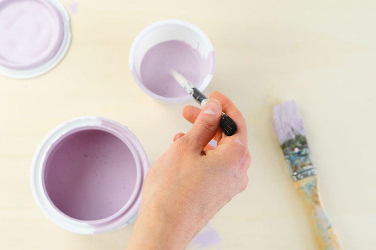 High angle view of hand dipping paintbrush in bucket