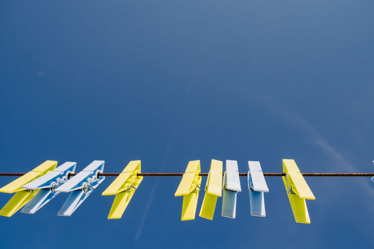 Low angle view of clothespins on clothesline against blue sky