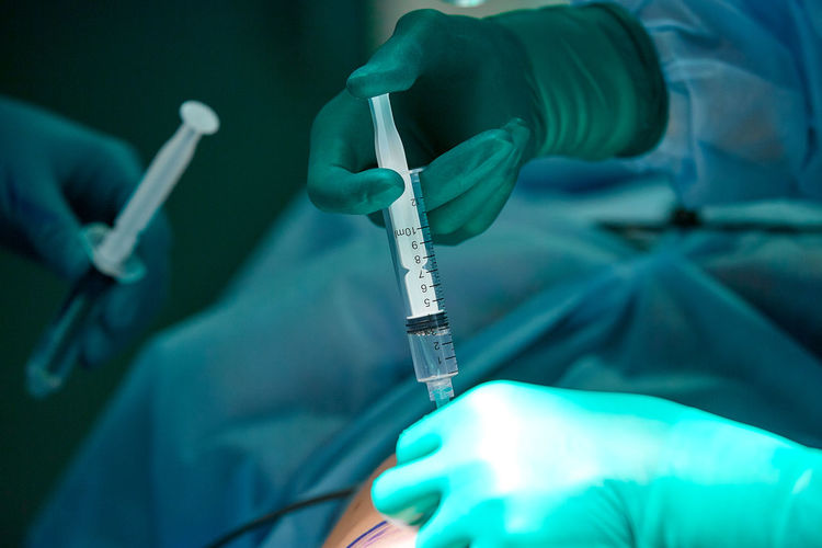Cropped hands of surgeon giving injection to patient at operating room