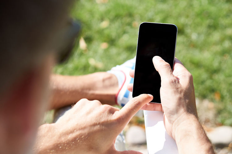 Cropped image of man using blank phone while sitting outdoors