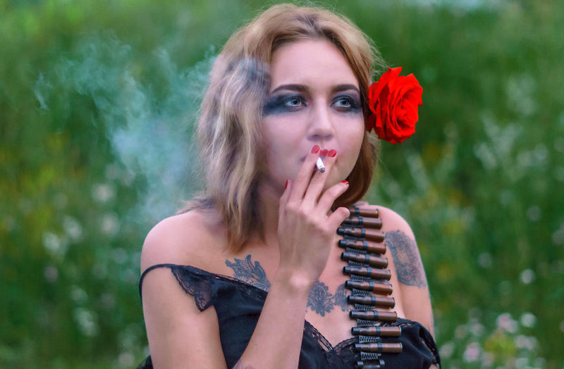 Beautiful young woman with cartridge belt smoking cigarette