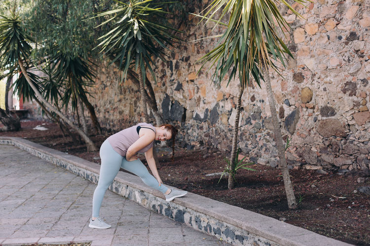 Side view of woman stretching against trees
