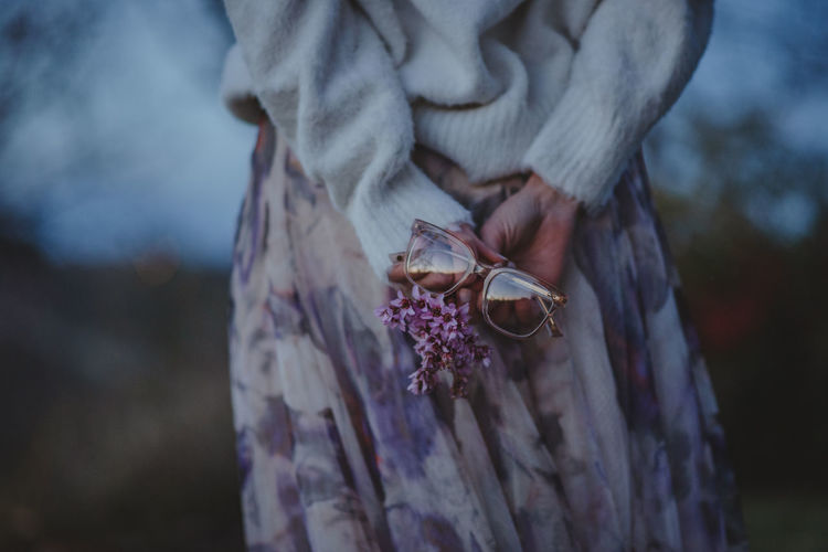 Close-up of hand holding purple flower and eyeglasses