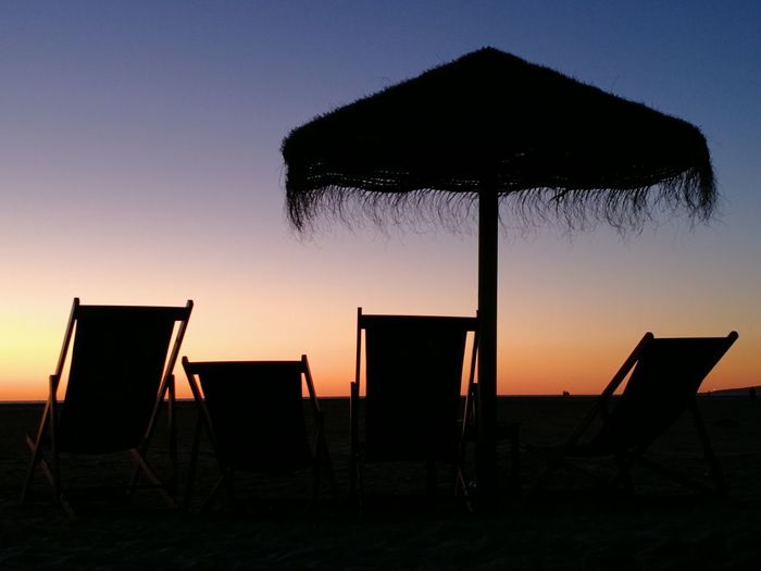 Silhouette chairs on beach against clear sky during sunset