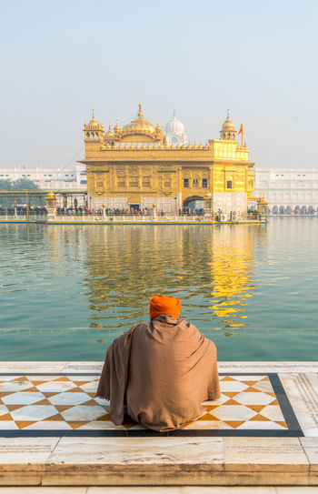 Rear view of man praying against golden temple amidst standing water