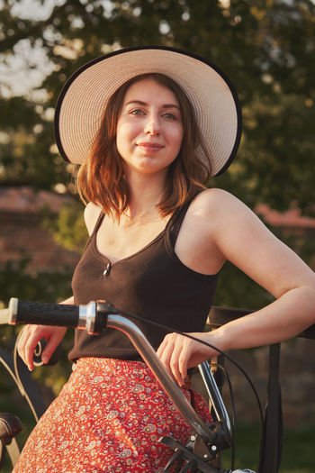 Portrait of smiling young woman standing by bicycle outdoors