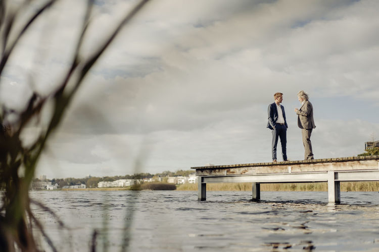 Two businessmen standing on jetty at a lake talking