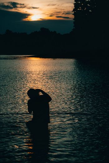 Silhouette man standing by lake against sky during sunset