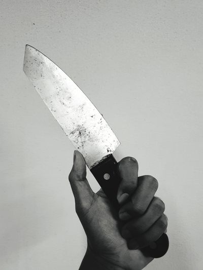 Close-up of hand holding knife against white background