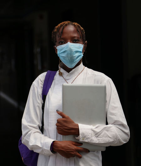 A black female afeica  student carrying a laptop and wearing a facemask.