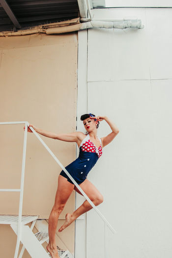 Portrait of young woman standing on stairs saluting wearing red white and blue swimwear
