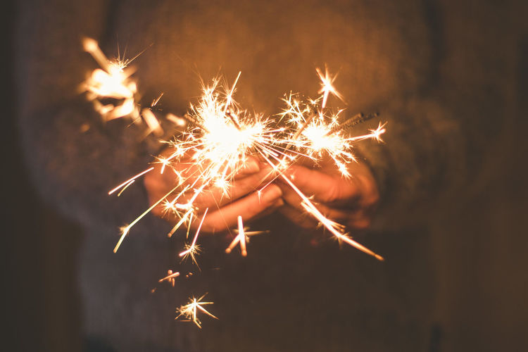 Midsection of woman holding lit sparkler at night