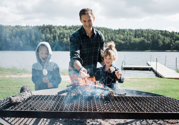 Father toasting marshmallows with his kids at the beach on a bbq
