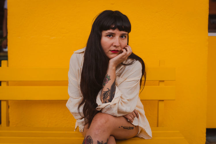 Young woman sitting against yellow wall