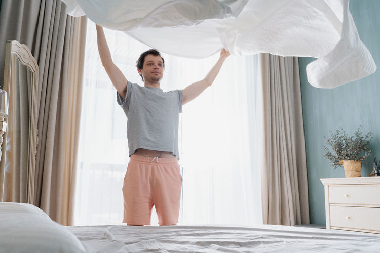 Adult man is putting the bedding cover or mattress pad on the bed. regular bed linen change