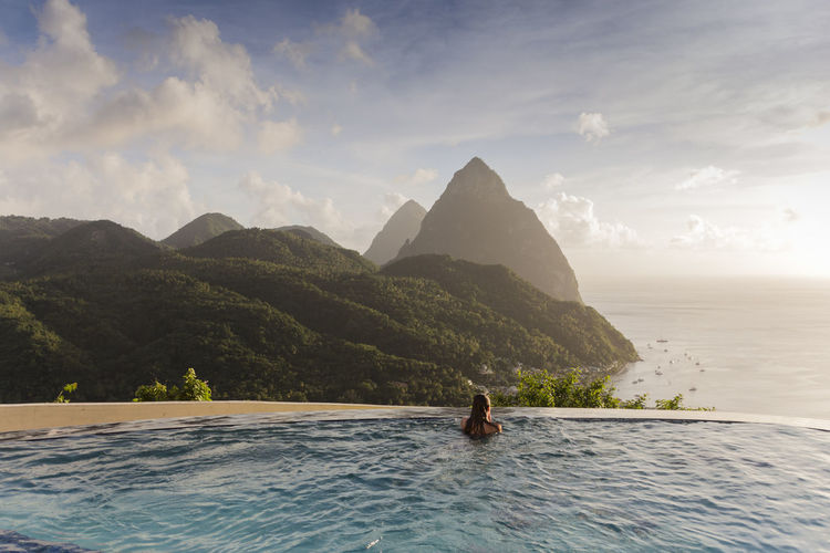 Scenic view of infinity pool with woman relaxing against sky