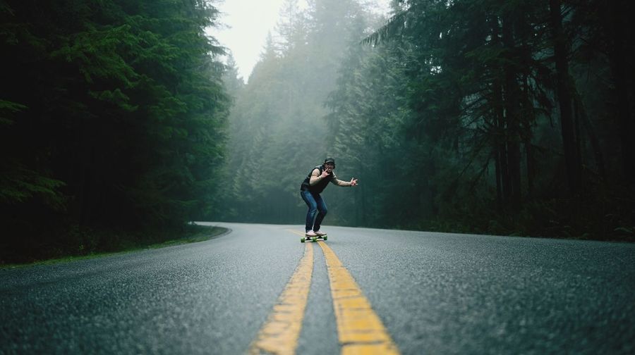 Man skateboarding on road amidst trees in forest