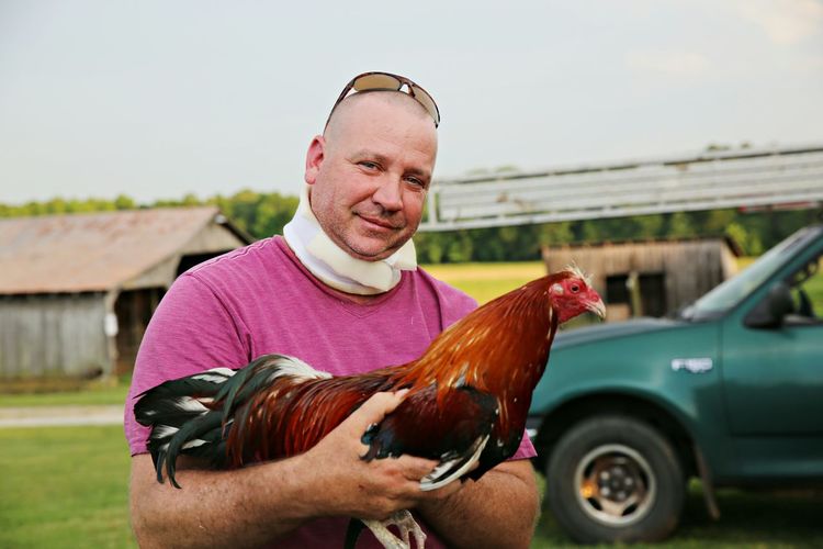 Portrait of man holding rooster against car