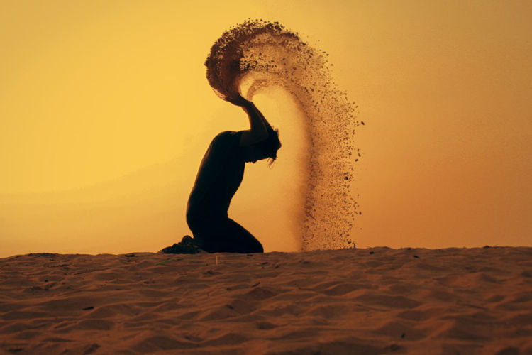 Silhouette man throwing sand against sky during sunset