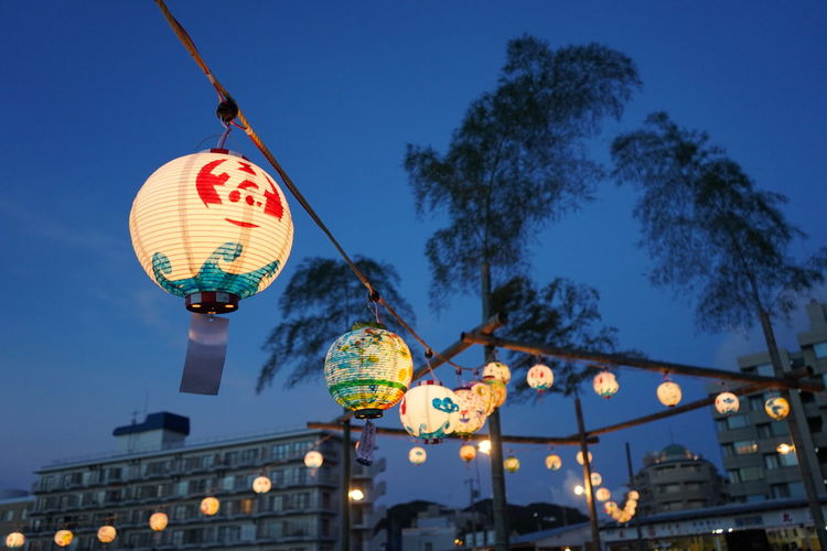 Low angle view of illuminated lanterns hanging against blue sky