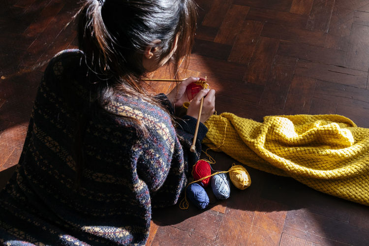 Young woman knitting wool on wooden floor at home