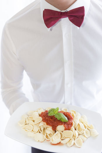 Midsection of waiter with pasta on plate against white background