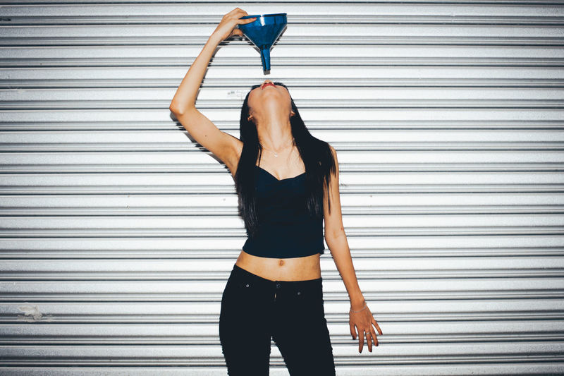 Young woman standing with funnel against corrugated iron at night