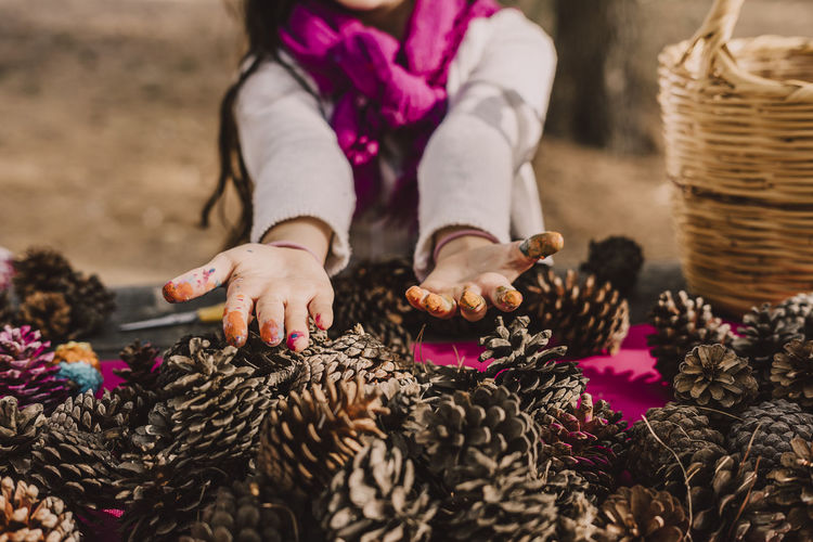 Messy hands of girl with pine cones at picnic table in park