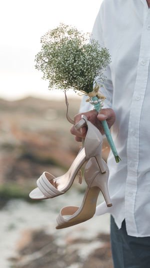Midsection of man holding bouquet and high heels