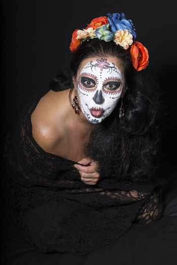 Close-up of woman with face paint sitting over black background