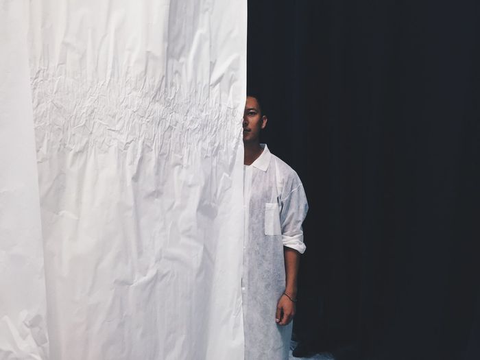Portrait of young man standing behind curtain