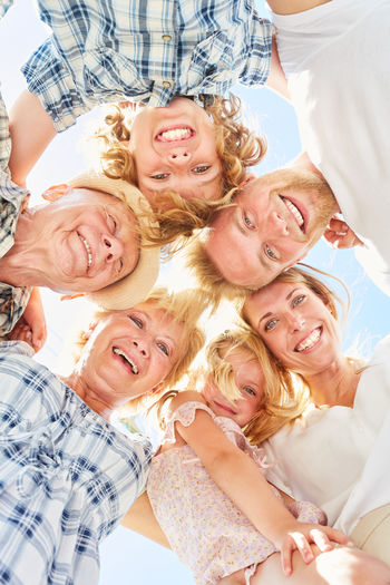 Low angle view of multi-generation family smiling in huddle against sky