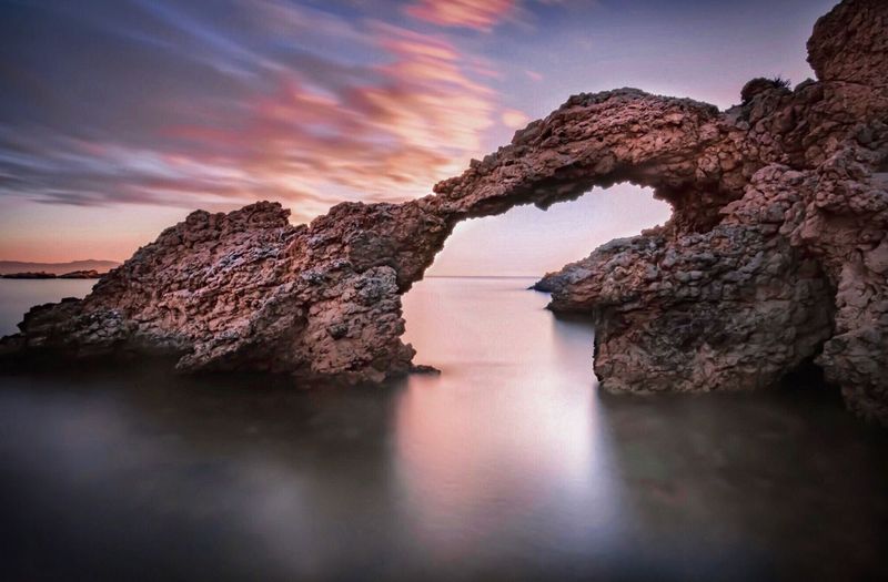 Rock formation in sea against sky during sunset