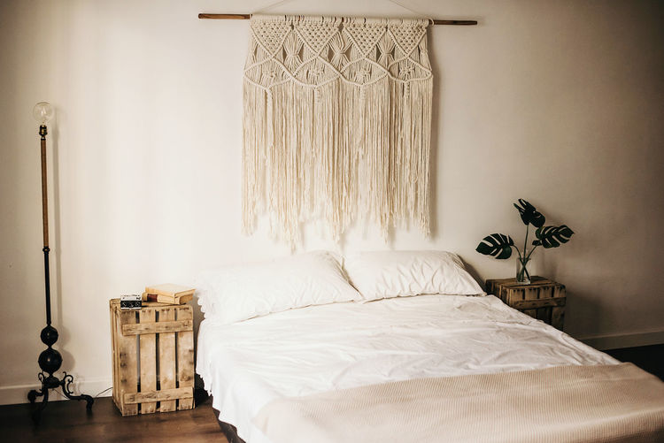 Vintage macrame decoration hanging on wall over comfortable bed in cozy bedroom at home