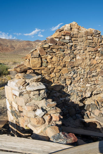 Rocks in tumbled down wall rubble abandoned stone cabin in desert mountain background against sky