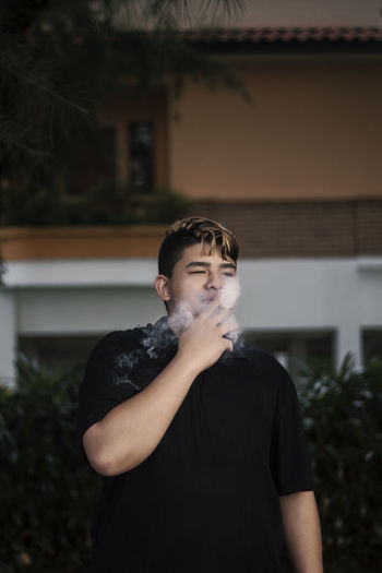 Overweight young man smoking cigarette in city