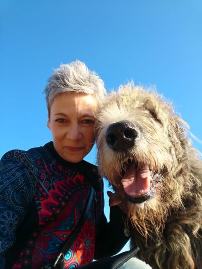 Low angle portrait of smiling woman with dog against blue sky