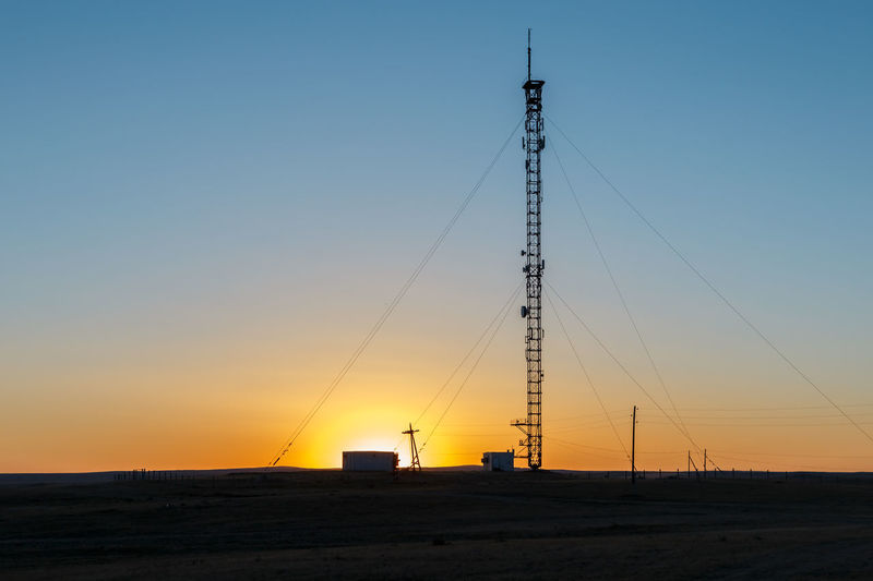 Electricity pylon on land against clear sky during sunset