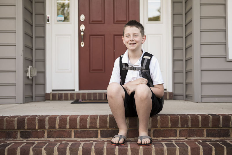 Tween boy with braces sits on brick front step, first day of school